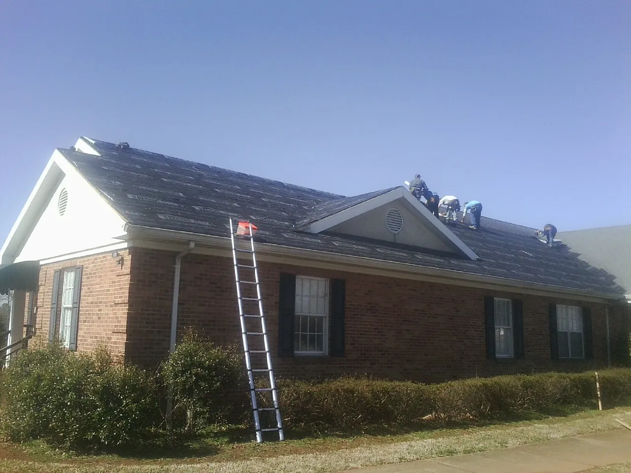 Crew tearing shingles off a brick ranch roof with a ladder set — Emergency Roof Repair work by our crew in Rancocas