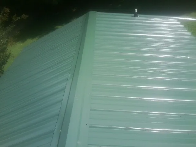 New green metal panels meeting at the ridge of a roof — Flat Roof Repair work by our crew in Rancocas