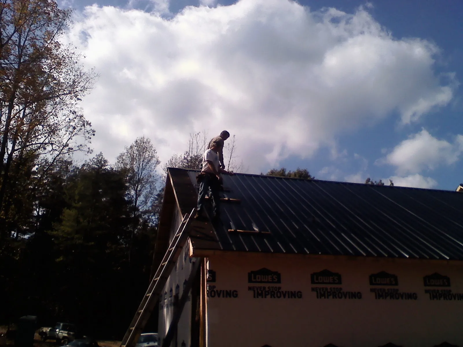 Roofer fastening dark metal panels high against a cloudy sky, from a Roof Inspection job in Rancocas