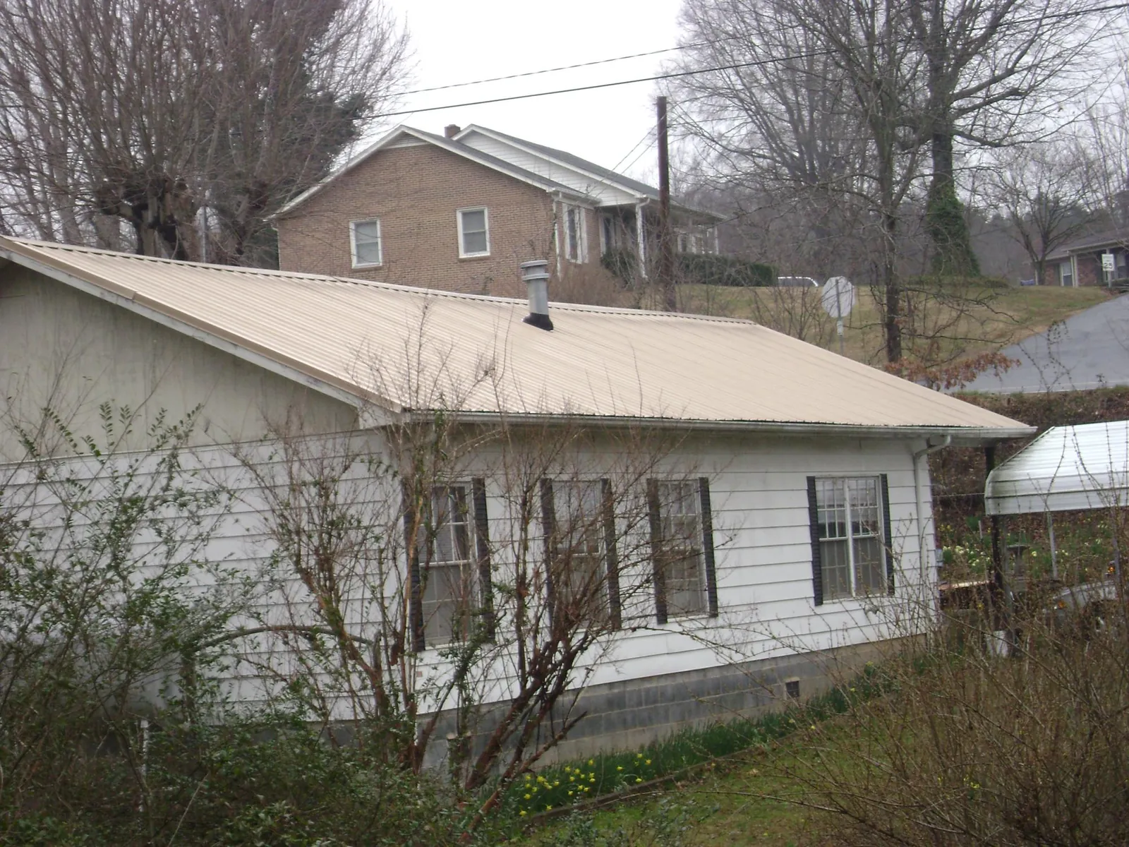 Tan metal roof on a white sided house set into a hillside — Commercial Roofing by Roofing Brothers in Rancocas
